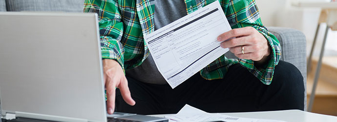 man reviewing paperwork at his laptop computer