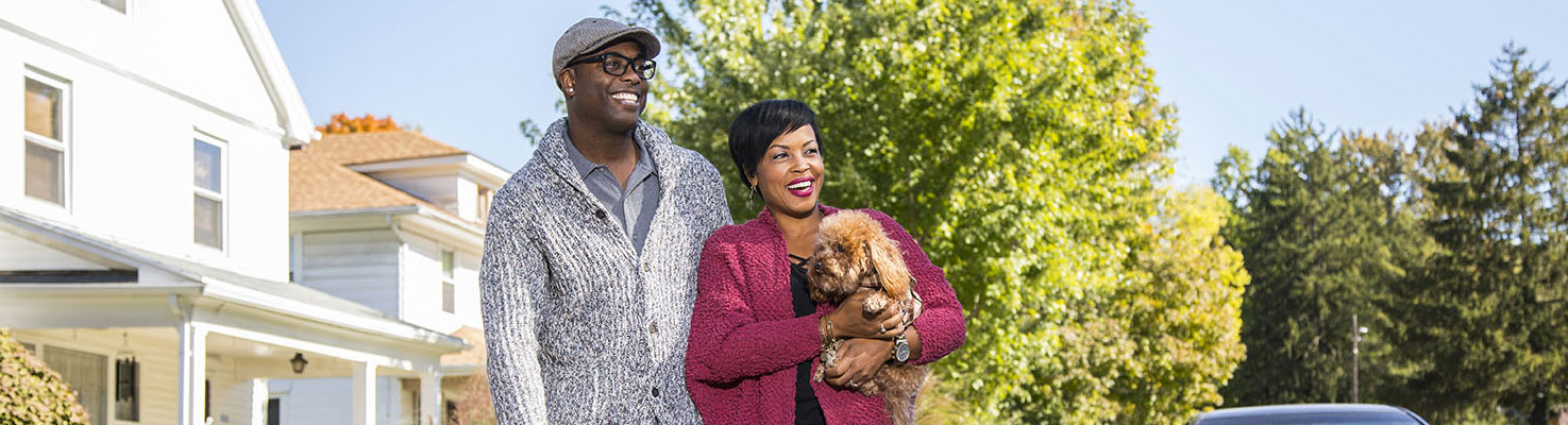 husband and wife standing outside holding their small dog